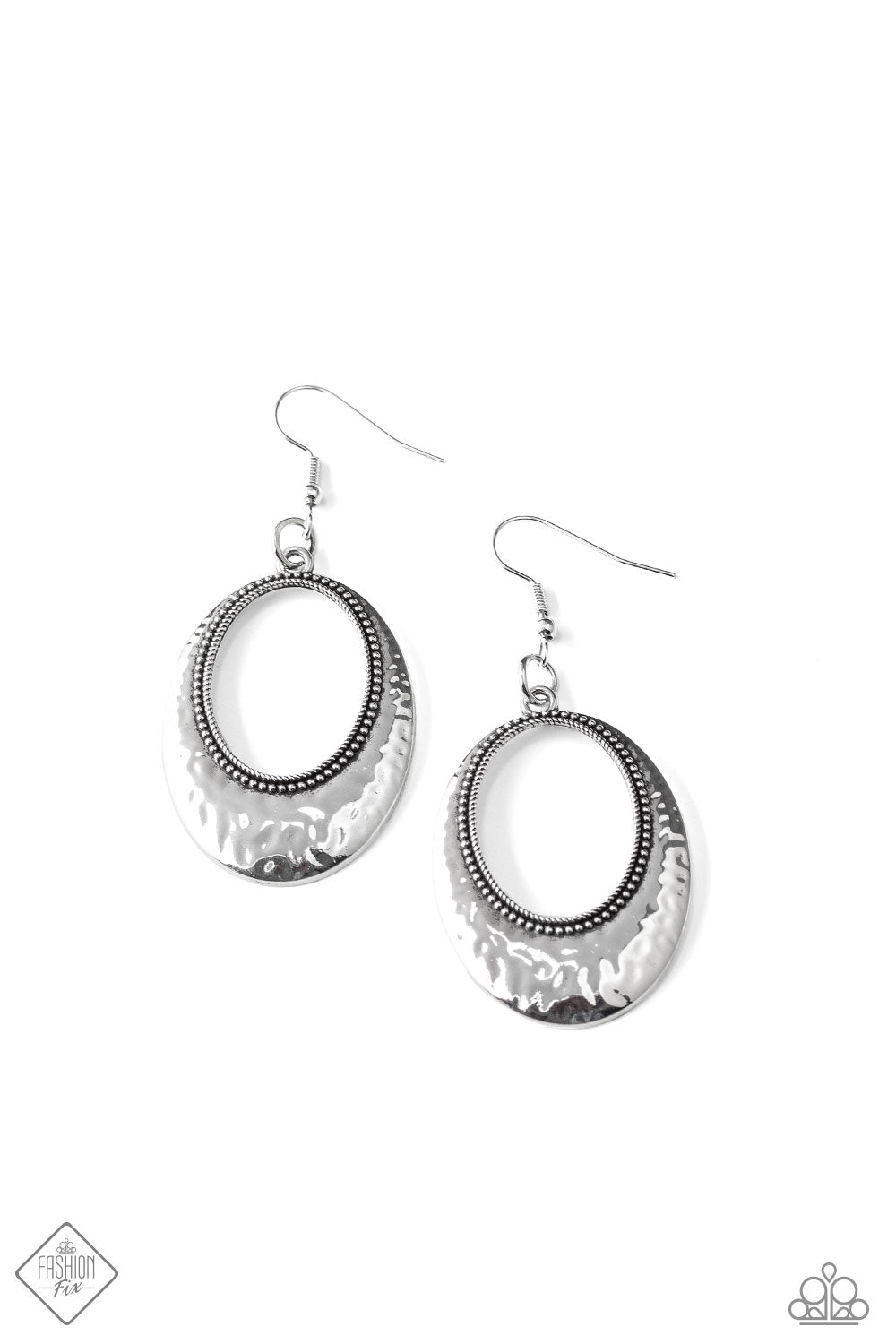 A hammered silver oval flares around a studded silver ring, creating a rustic frame. The subtle beveled curve of the frame allows the light to catch at every angle, emphasizing the high-sheen finish. Earring attaches to a standard fishhook fitting. Sold as one pair of earrings.