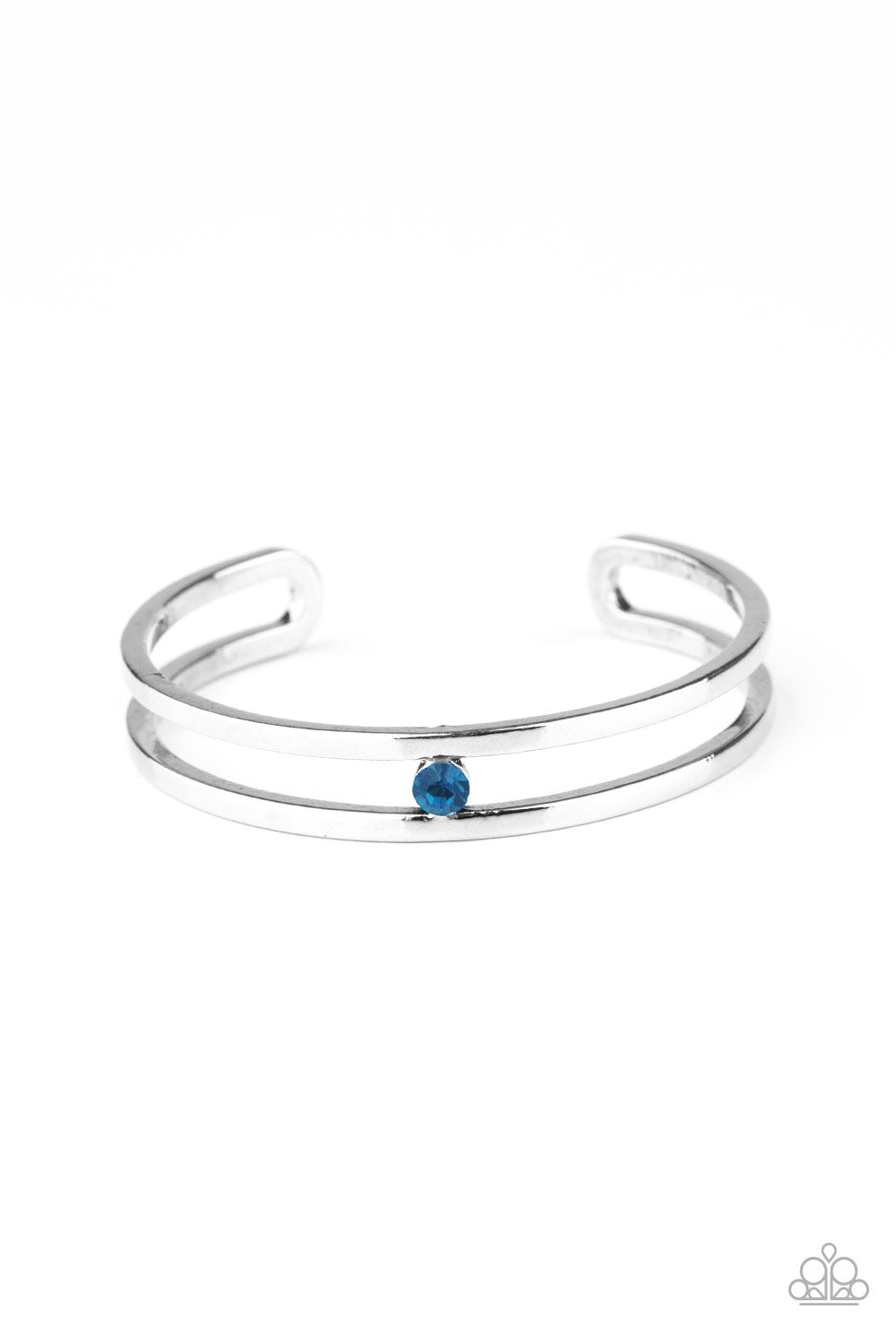 A dainty blue rhinestone is nestled inside the center of an airy silver cuff, adding a glittery pop of color to the wrist. Sold as one individual bracelet.