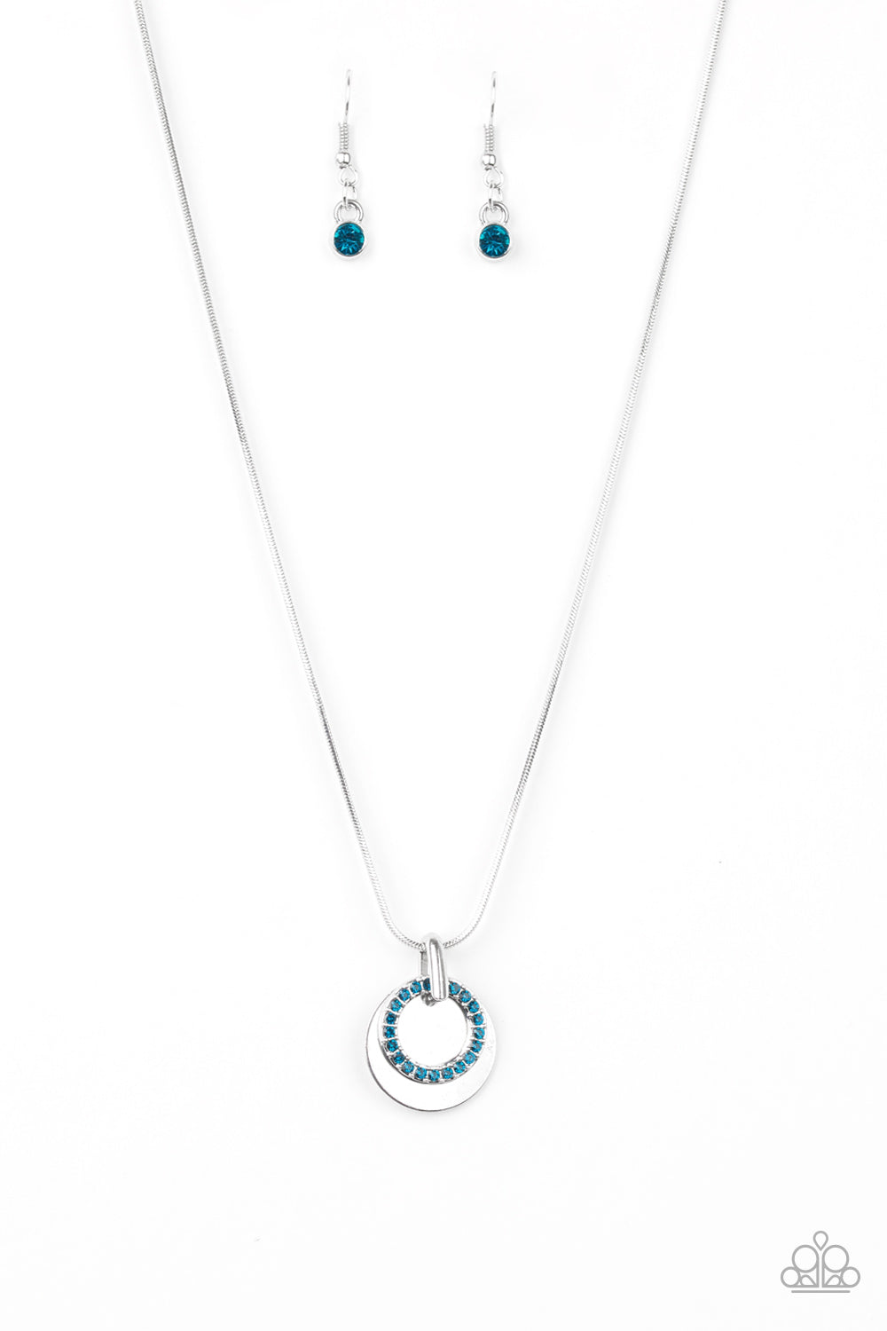 A glistening silver disc and a blue rhinestone encrusted ring slide along a sleek silver chain, coalescing into a refined pendant below the collar. Features an adjustable clasp closure. Sold as one individual necklace. Includes one pair of matching earrings.