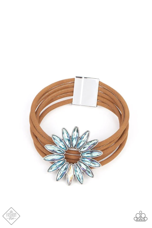 Row after row of brown suede cords layer around the wrist. Featuring oblong marquise style cuts, an iridescent collection of rhinestones fans out into a circular focal point, resulting in a celestial centerpiece. Features a magnetic closure. Due to its prismatic palette, color may vary. Sold as one individual bracelet.
