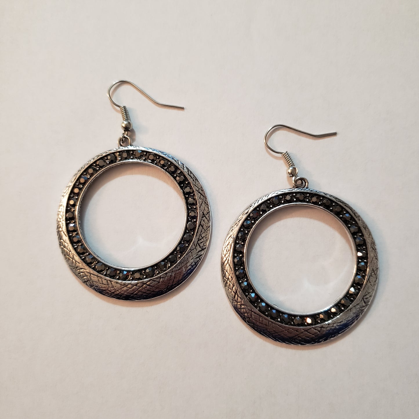 Delicately scratched in antiqued shimmer, a glistening silver hoop is encrusted in a ring of glittery hematite rhinestones for a refined look. Earring attaches to a standard fishhook fitting. Sold as one pair of earrings.