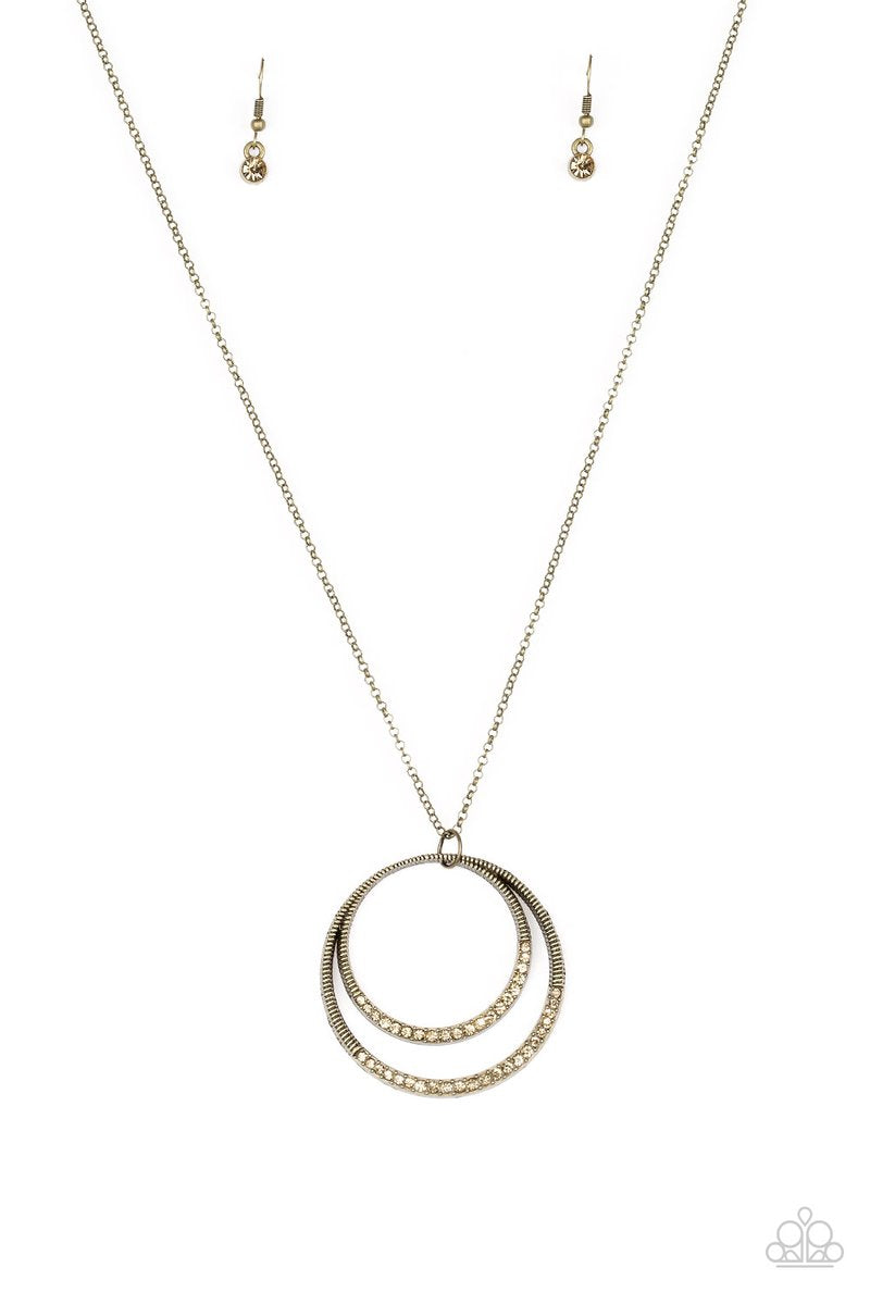 A daring circular pendant swings from the bottom of an elongated brass chain for a refined look. The bottoms of the ornate brass pendant are encrusted in golden topaz rhinestones for a glamorous finish. Features an adjustable clasp closure. Sold as one individual necklace. Includes one pair of matching earrings.