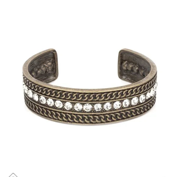 A row of sparkling white rhinestones, surrounded by studded texture, is bordered by an intricate chain-like motif etched in antiqued brass. The contrast of sparkle and grit results in an unapologetically industrial cuff that wraps boldly around the wrist. Sold as one individual bracelet.