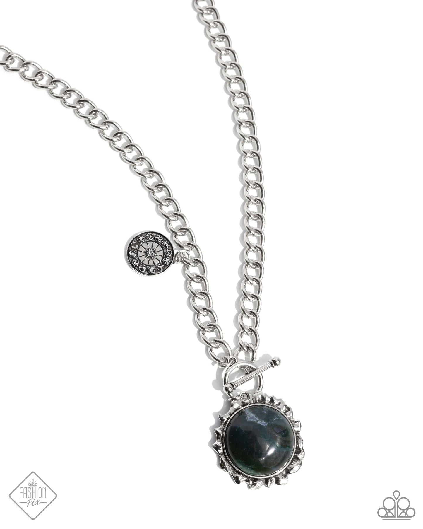 Set in a silver sun-bordered frame, a round green marbled stone radiates from a thick silver chain below the neckline. Stamped with the zodiac chart, an antiqued silver pendant swings along the chain above the stone for an astrological finish. Features a toggle closure. As the stone elements in this piece are natural, some color variation is normal. Sold as one individual necklace. Includes one pair of matching earrings.