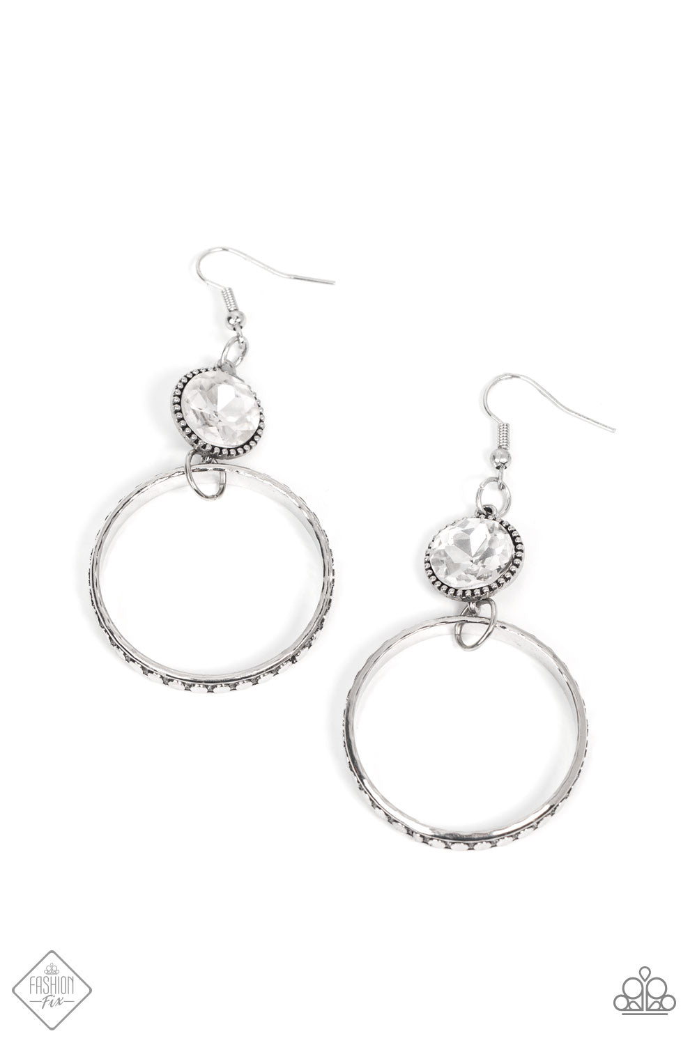 The outer edge of a silver ring is stamped with a flattened dot motif as it swings below a dramatic white rhinestone that sparkles inside a daintily dotted antiqued silver frame, creating an upscale, edgy modern lure. Earring attaches to a standard fishhook fitting. Sold as one pair of earrings.