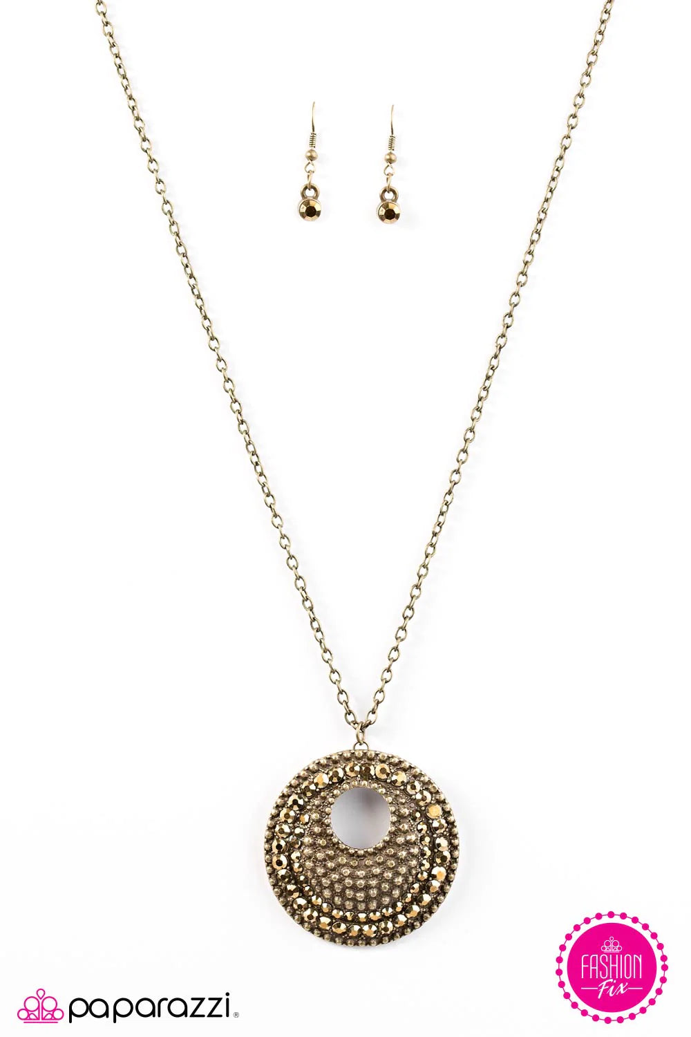 Embossed in studded textures, a beveled brass pendant swings from the bottom of an elongated brass chain in a dramatic fashion. Glittery aurum rhinestones are haphazardly sprinkled across the frame, adding edgy metallic accents to the tactile palette. Features an adjustable clasp closure. Sold as one individual necklace. Includes one pair of matching earrings.