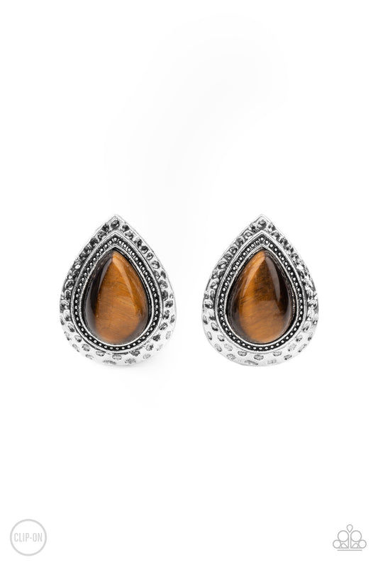A teardrop Tiger's Eye stone is pressed into the center of a hammered silver frame, creating a rustic display. Earring attaches to a standard clip-on fitting.  Sold as one pair of clip-on earrings.