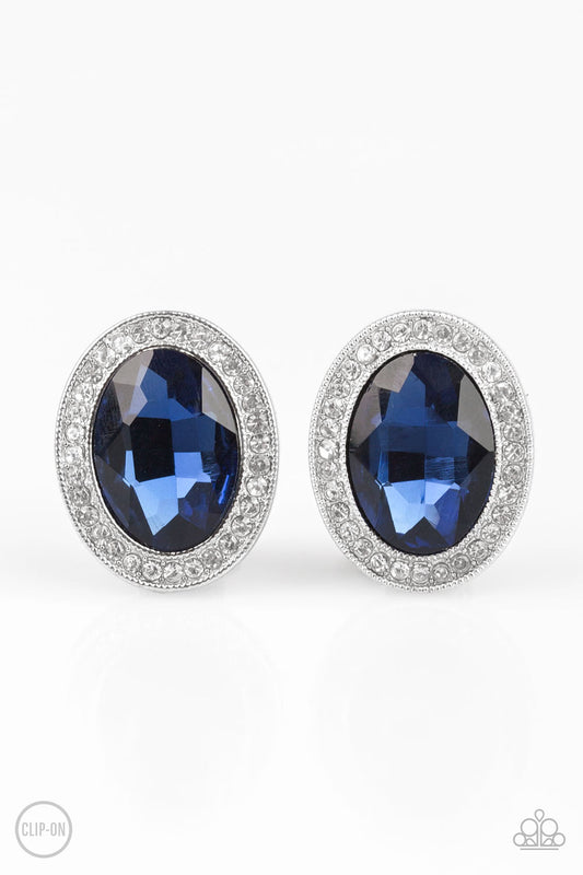 An oversized blue gem is pressed into the center of a silver frame radiating with glassy white rhinestones for a glamorous look. Earring attaches to a standard clip-on fitting.  Sold as one pair of clip-on earrings.
