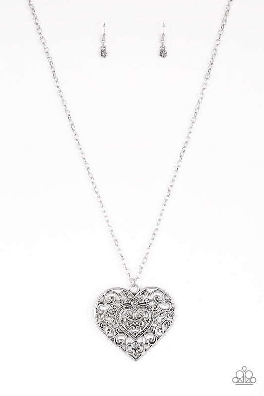Dotted with smoky rhinestones, an oversized heart frame radiating with glistening filigree detail swings from the bottom of a lengthened silver chain for a vintage inspired look. Features an adjustable clasp closure.  Sold as one individual necklace. Includes one pair of matching earrings.