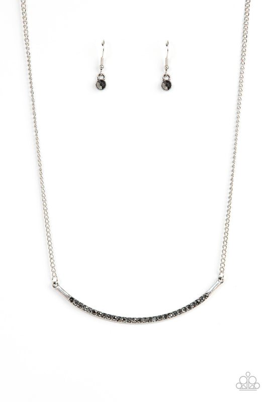 Encrusted in smoky hematite rhinestones, a curved silver bar bows below the collar for a smoldering style. Features an adjustable clasp closure.  Sold as one individual necklace. Includes one pair of matching earrings.