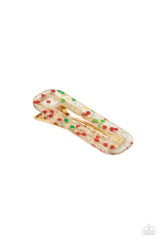 A shimmery collection of red, green, and gold confetti and dainty sparkles are encased in a clear acrylic frame atop a gold frame. Features a standard hair clip on the back.