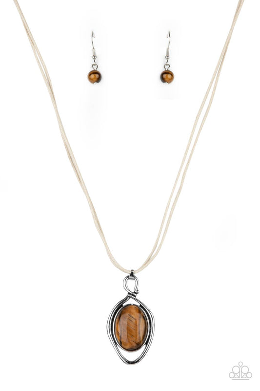An oversized tiger's eye stone is pressed into a silver oval frame and outlined with an unexpected irregular shaped frame. The eye-catching pendant suspends from a double strand of white cord below the collar for a mysterious finish. Features an adjustable clasp closure.  Sold as one individual necklace.