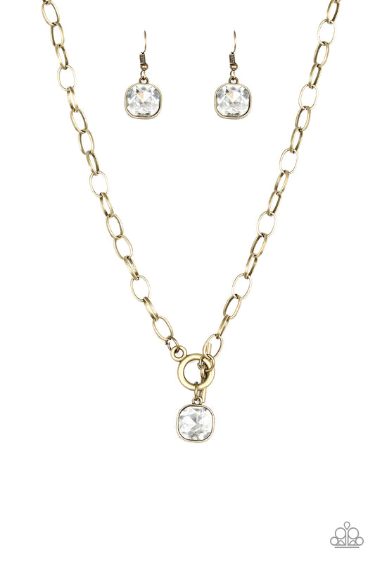 Pressed into a sleek brass frame, a dramatic white gem swings from the bottom of a glistening brass chain below the collar for a chic look. Features a toggle closure.  Sold as one individual necklace. Includes one pair of matching earrings.