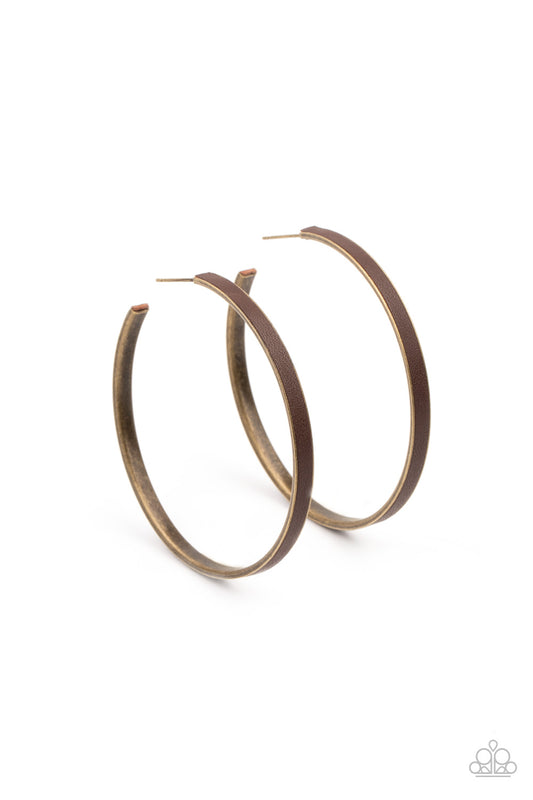 A brown leather lace is pressed along the indented spine of a brass hoop, creating a bold pop of color. Earring attaches to a standard post fitting. Hoop measure approximately 2 1/4" in diameter.  Sold as one pair of hoop earrings.