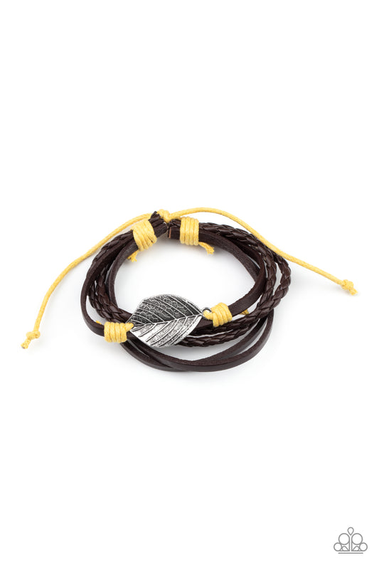 A lifelike silver leaf frame is knotted in place with yellow cording across the front of a dainty brown leather band. Matching plain and braided leather bands join the centerpiece, creating earthy layers around the wrist. Features an adjustable sliding knot closure.  Sold as one individual bracelet.