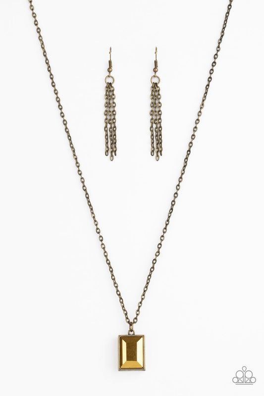 Featuring an emerald style cut, a faceted aurum gem is pressed into a sleek brass frame at the bottom of a dainty brass chain below the collar for an edgy look. Features an adjustable clasp closure.  Sold as one individual necklace. Includes one pair of brass fringe earrings.