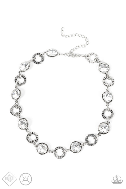Dramatic white gems encased in daintily dotted frames link with silver rings finished with flattened studded texture. The stunning rhinestones and edgy rings alternate around the neck, resulting in an upscale industrial flair. Features an adjustable clasp closure.  Sold as one individual choker necklace. Includes one pair of matching earrings.