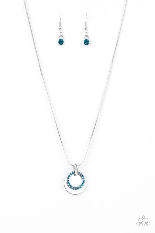 A glistening silver disc and a blue rhinestone encrusted ring slide along a sleek silver chain, coalescing into a refined pendant below the collar. Features an adjustable clasp closure.  Sold as one individual necklace. Includes one pair of matching earrings.