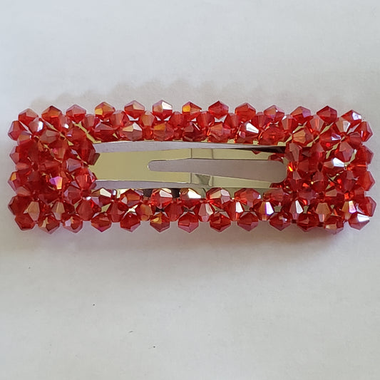 Featuring an iridescent shimmer, faceted red crystal-like beads bedazzle the front of a rectangular hair clip for a sparkly finish. Features a standard snap clip on the back.  Sold as one individual hair clip.