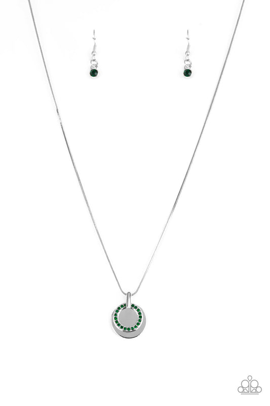 A glistening silver disc and a green rhinestone encrusted ring slide along a sleek silver chain, coalescing into a refined pendant below the collar. Features an adjustable clasp closure.  Sold as one individual necklace. Includes one pair of matching earrings.