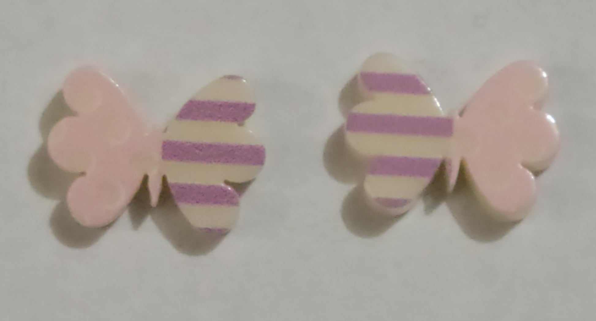 Colorful earrings in assorted colors and shapes. Featuring one striped and one polka dotted wing, the colorful butterfly frames vary in shades of pink and purple stripes. Earrings attach to standard post fittings.  Sold as one pair of post earrings.