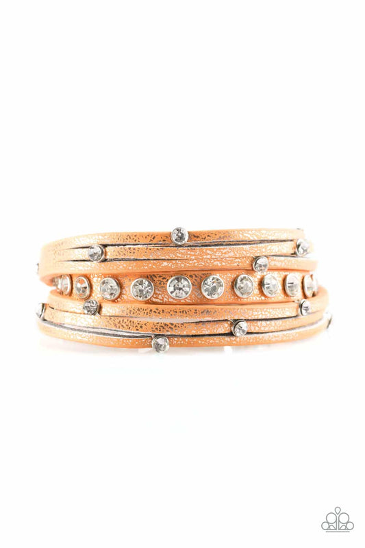 Dusted in a golden shimmer, a skinny strip of orange leather is spliced into sections of glittery strands. Infused with white rhinestones, the elongated band double wraps around the wrist for a fierce one-of-a-kind look. Features an adjustable snap closure.  Sold as one individual bracelet.