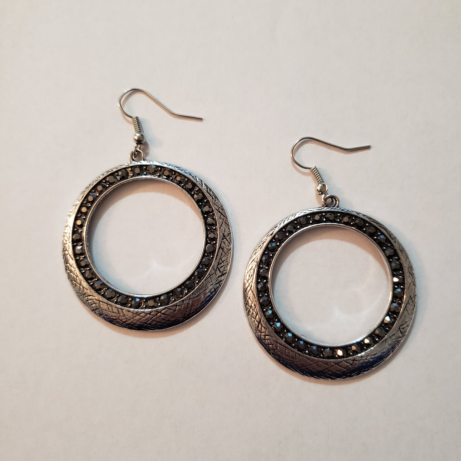 Delicately scratched in antiqued shimmer, a glistening silver hoop is encrusted in a ring of glittery hematite rhinestones for a refined look. Earring attaches to a standard fishhook fitting.  Sold as one pair of earrings.