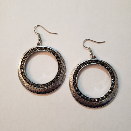 Delicately scratched in antiqued shimmer, a glistening silver hoop is encrusted in a ring of glittery hematite rhinestones for a refined look. Earring attaches to a standard fishhook fitting.  Sold as one pair of earrings.