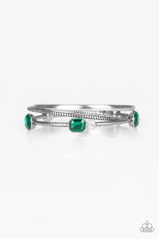 Brushed in an antiqued shimmer, a collection of smooth and textured silver bangles stack across the wrist. Varying in shape and size, glittery green and white rhinestones are encrusted along one bangle for a glamorous glow.  Sold as one set of three bracelets.