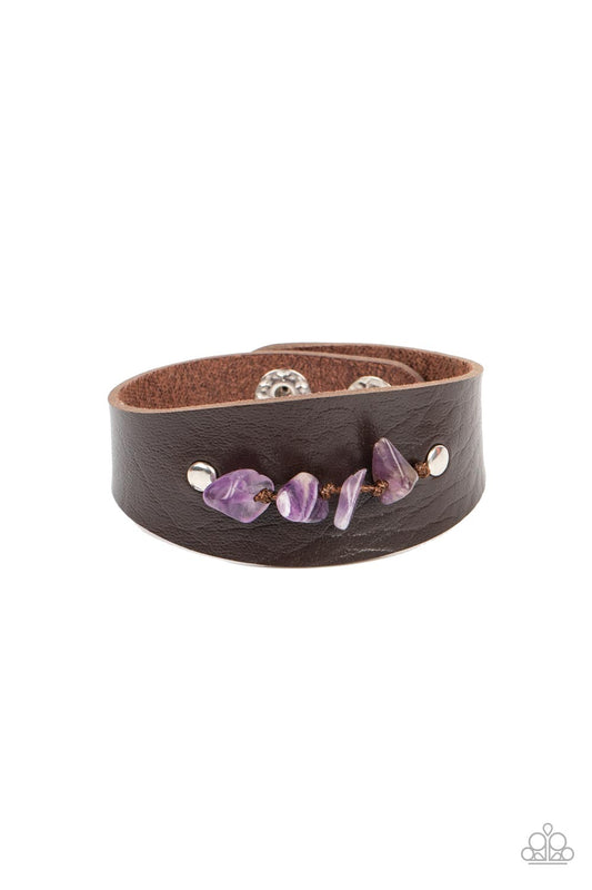 Pieces of amethyst pebbles are threaded along a brown cord that is studded in place across the front of a rounded leather band, resulting in an earthy pop of color atop the wrist. Features an adjustable snap closure.  Sold as one individual bracelet.