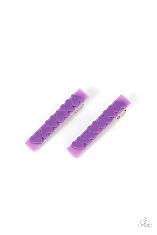 A row of purple hearts alternate across the front of a light purple rectangular frame, creating a charming pair of flirtatious hair clips. Features standard hair clips on the back.  Sold as one pair of hair clips.