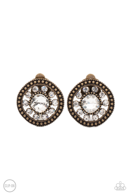 Featuring an oversized center, a white rhinestone encrusted flower blooms across the brass center of a studded frame for a sparkly finish. Earring attaches to a standard clip-on fitting.  Sold as one pair of clip-on earrings.