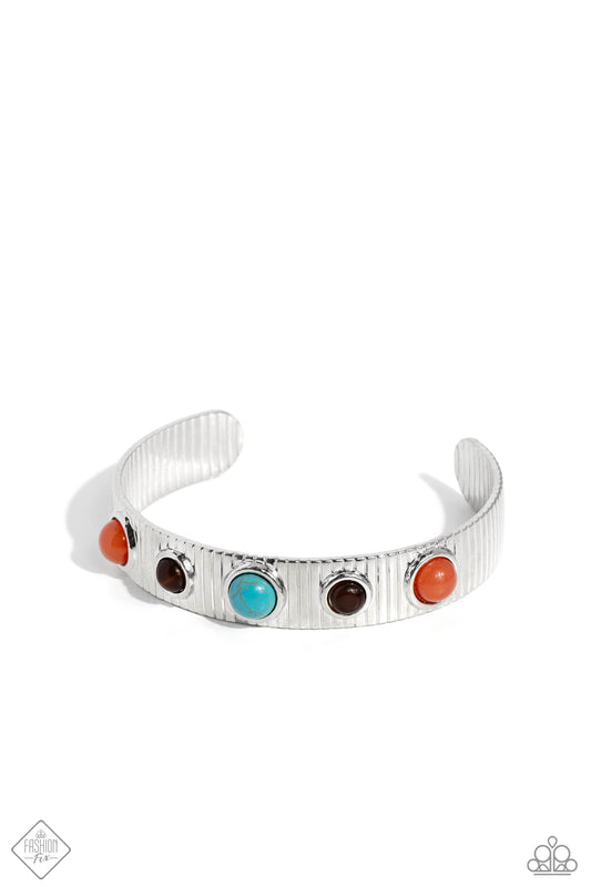 Pressed in round, elevated silver frames, a collection of Burnt Sienna, brown cat's eye, and turquoise stone beads dot along the front of a linear-textured silver cuff for a desert-patterned display. As the stone elements in this piece are natural, some color variation is normal.  Sold as one individual bracelet.