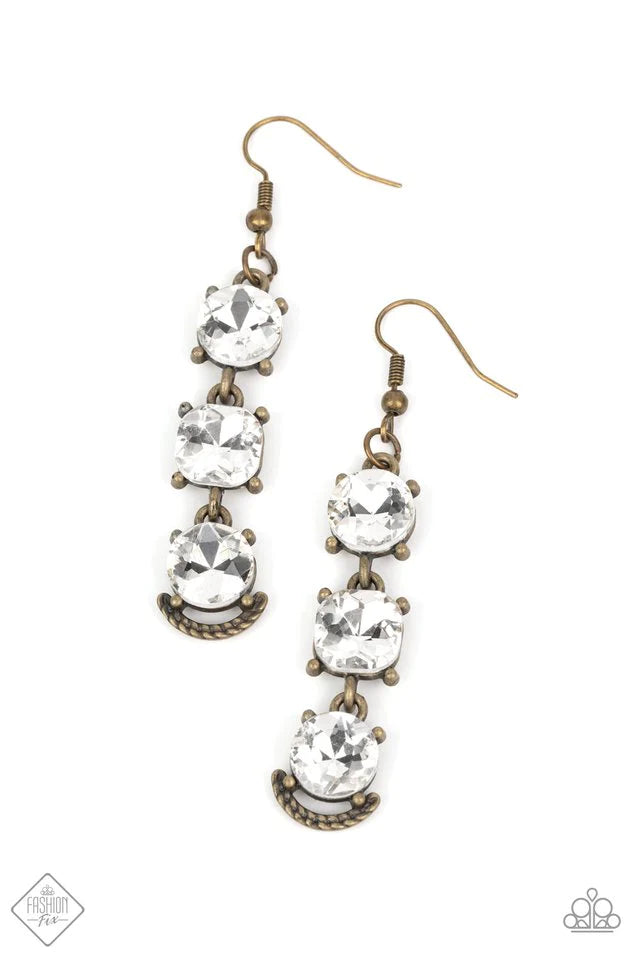 A trio of bold white rhinestones, set in pronged antiqued brass fittings, stack one above the other. The center rhinestone is almost imperceptibly square rather than round and the final rhinestone is accented with a gritty metallic crescent etched with ropelike texture, creating a ruggedly glamorous lure. Earring attaches to a standard fishhook fitting.  Sold as one pair of earrings.