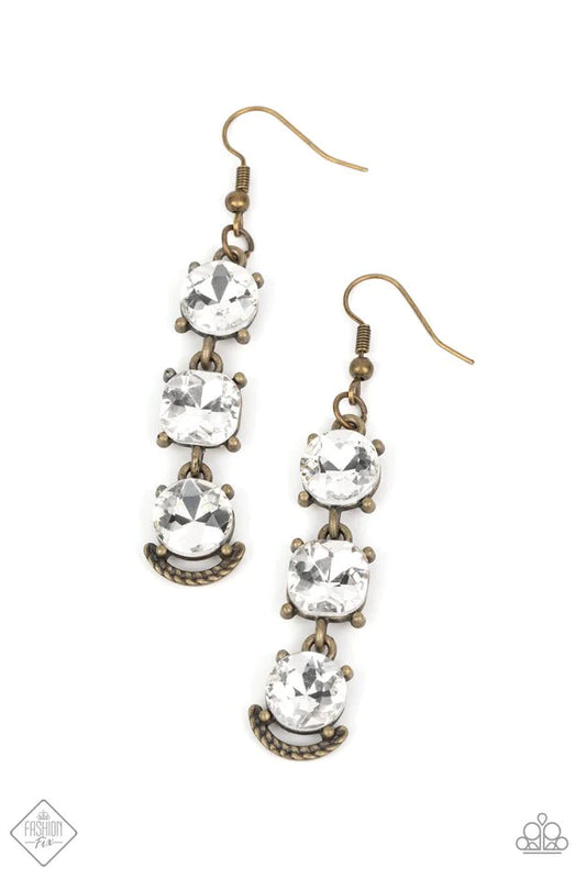 A trio of bold white rhinestones, set in pronged antiqued brass fittings, stack one above the other. The center rhinestone is almost imperceptibly square rather than round and the final rhinestone is accented with a gritty metallic crescent etched with ropelike texture, creating a ruggedly glamorous lure. Earring attaches to a standard fishhook fitting.  Sold as one pair of earrings.