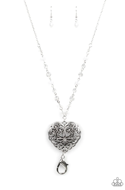 Featuring opaque and glassy crystal-like finishes, a dainty collection of white beads gives way to an oversized filigree filled heart frame, creating an antiqued locket inspired pendant at the bottom of a lengthened silver chain. Features an adjustable clasp closure.  Sold as one individual necklace. Includes one pair of matching earrings.