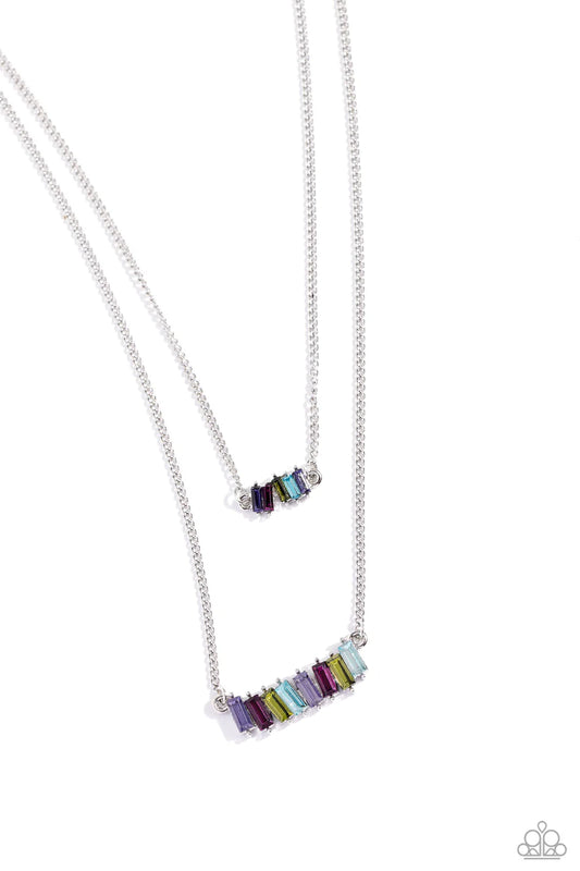 Two strands of dainty silver chains fall into tiered layers as they cascade down the chest. Featuring various multicolored shades, emerald-cut gems set in silver-pronged fittings dance along each chain for a dizzying display. Features an adjustable clasp closure.  Sold as one individual necklace. Includes one pair of matching earrings.