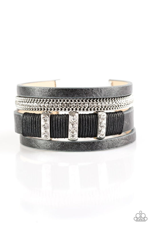 Paparazzi Accessories Bracelet:  Metallic black leather strands layer across the wrist. Infused with silver chain and white rhinestone accents, black cording knots around a leather strand, securing glittery white rhinestone frames in place for a sassy finish. Features an adjustable clasp closure.  Sold as one individual bracelet.