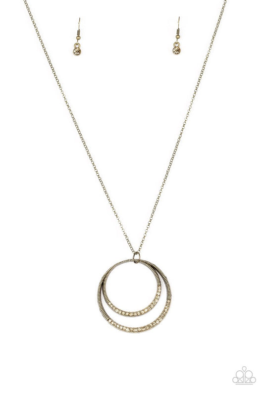 A daring circular pendant swings from the bottom of an elongated brass chain for a refined look. The bottoms of the ornate brass pendant are encrusted in golden topaz rhinestones for a glamorous finish. Features an adjustable clasp closure.  Sold as one individual necklace. Includes one pair of matching earrings.