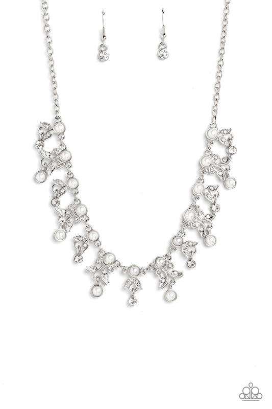 Infused along a classic silver chain, a row of white pearls, pressed into silver frames, stands out against the collar for a touch of refinement. Dangling below the row of white pearls, a shimmery collection of leaf-like filigree and detailing, studded with dainty white rhinestones and silver studs, adds a botanical element to the elegant display. Crystal-like white gems and white pearls encased in silver frames, dangle below every other botanical charm, rounding out the design with whimsical movement. 