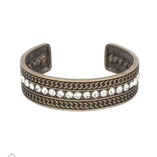 A row of sparkling white rhinestones, surrounded by studded texture, is bordered by an intricate chain-like motif etched in antiqued brass. The contrast of sparkle and grit results in an unapologetically industrial cuff that wraps boldly around the wrist.  Sold as one individual bracelet.