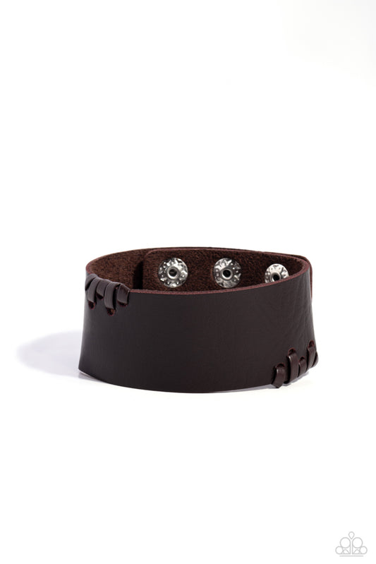 Sections of brown leathery laces are threaded along the edges of a thick brown leather band, resulting in an edgy display around the wrist.  Features an adjustable snap closure.   Sold as one individual bracelet.