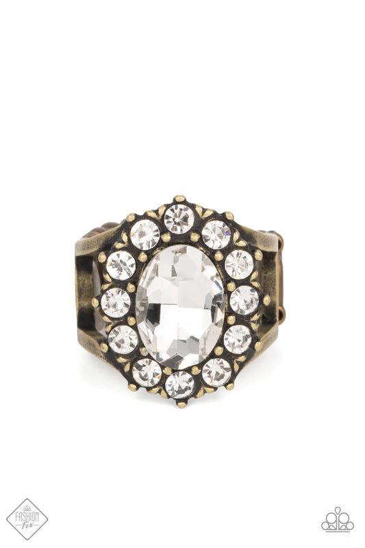 A dauntless oval rhinestone is encircled by dainty sparkling gems. Accented with petite antiqued brass studs, the dramatic design joins with an airy layered brass band to create a captivating arrangement atop the finger. Features a stretchy band for a flexible fit.  Sold as one individual ring.