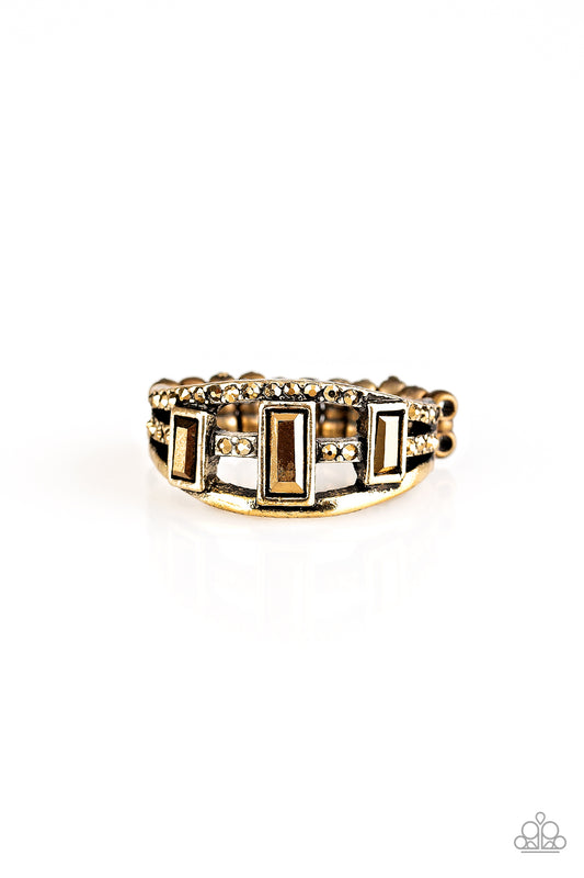 Three aurum emerald-cut rhinestones are encrusted along three brass bands radiating with smooth surfaces and sections of glittery aurum rhinestones for an edgy fashion. Features a stretchy band for a flexible fit.  Sold as one individual ring.
