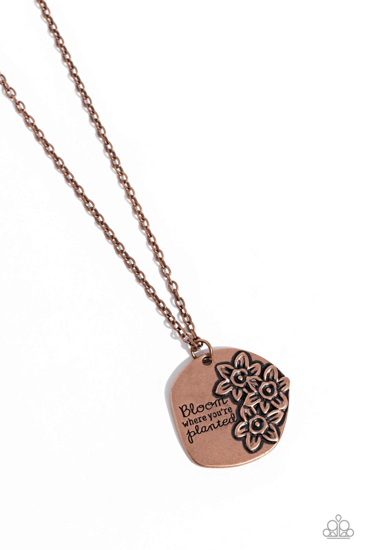 An asymmetrical copper pendant with a hammered finish, glides at the bottom of a dainty copper chain. Stamped on the pendant, the phrase "Bloom where you're planted" stands out on the asymmetrical surface in a curly, script font. Tactile, copper flowers bloom next to the phrase for a floral finish. Features an adjustable clasp closure.  Sold as one individual necklace. Includes one pair of copper fringe earrings.
